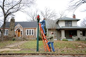 Staff Photo by Allison Kwesell Scott Harrison, top, and Ray Gross hang a wreath on a lightpole on Eveningside Drive at Ferger Place. Ferger Place is having a Christmas Tour of Homes in preperation for it's 100th anniversary next year.